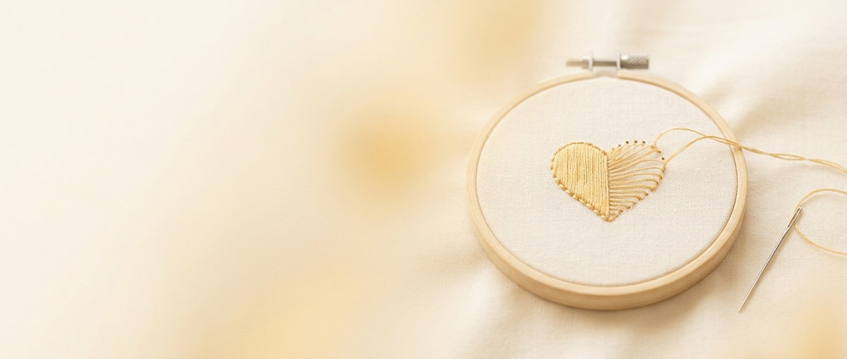 Bastidor de bordado con un corazón dorado a medio descoser sobre lino crema