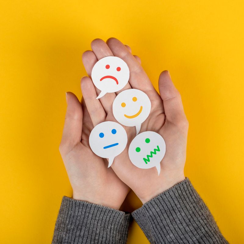 Manos sostienen caritas con distintas emociones, curso gratuito Del Síntoma al Equilibrio Emocional