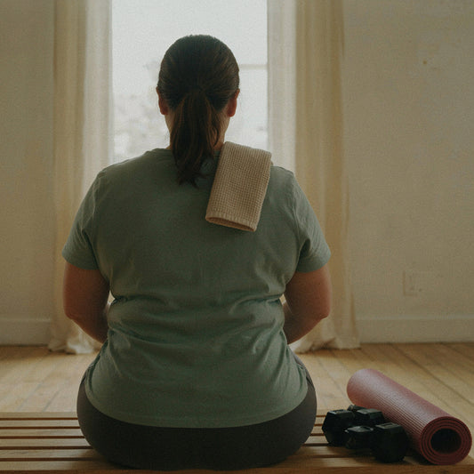 Mujer sentada de espaldas en un estudio de entrenamiento, descansando con una botella de agua entre las manos